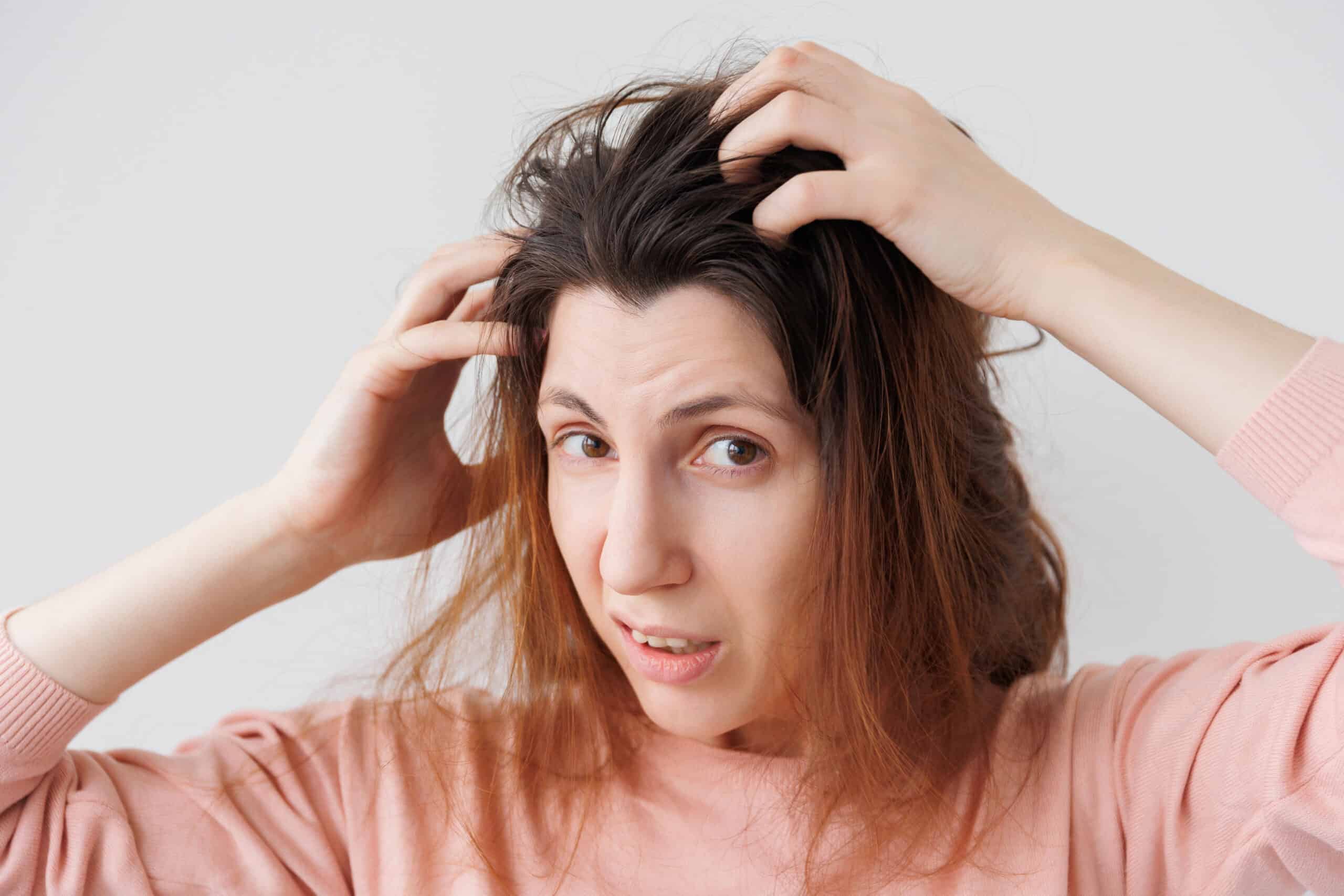 Woman scratching her scalp and looking uncomfortable, possibly due to itching or irritation.