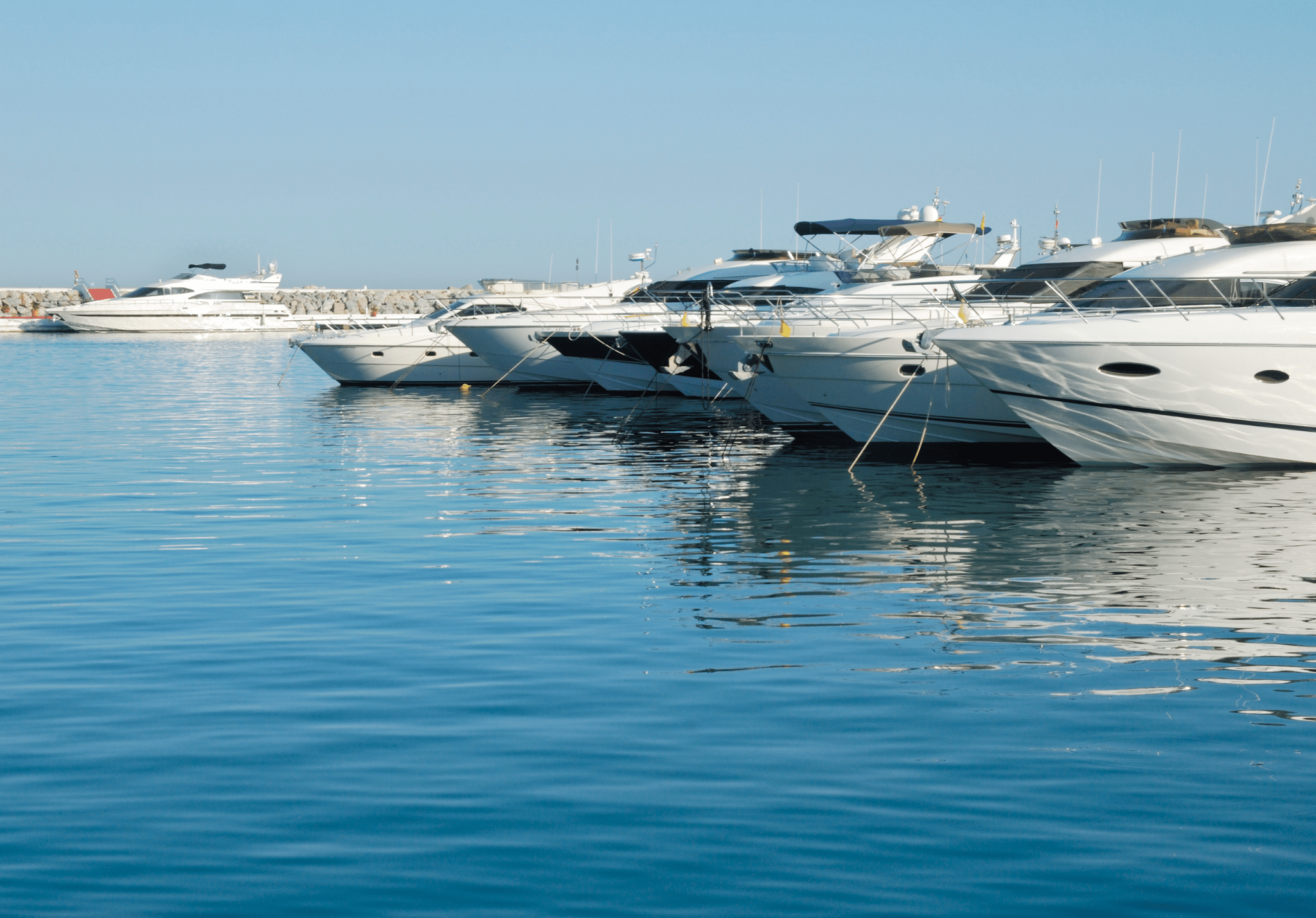 Multiple white and blue motorboats moored in calm blue water at a Mediterranean marina
