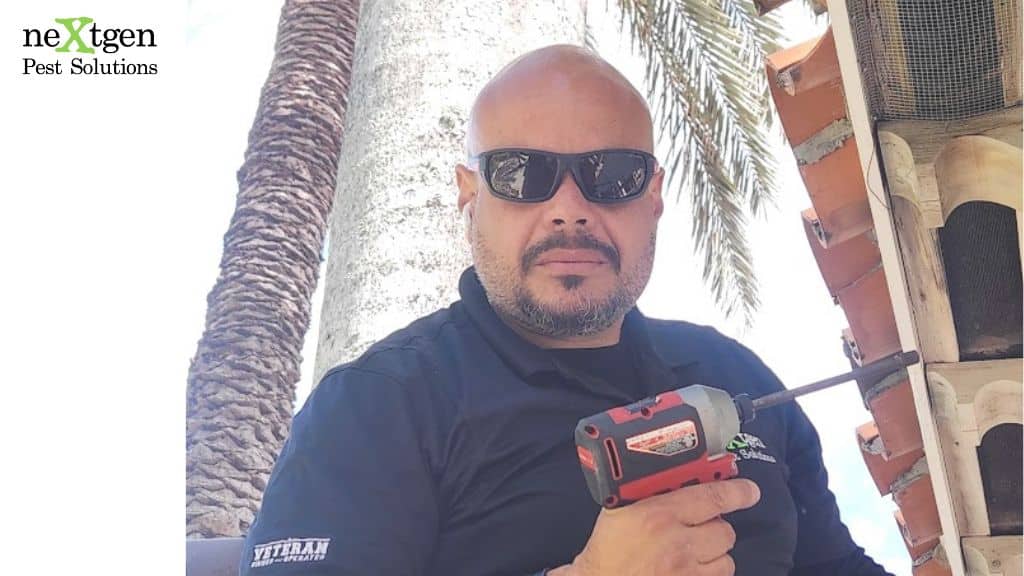 Pest control technician using a power tool while working on a home exterior near the roofline